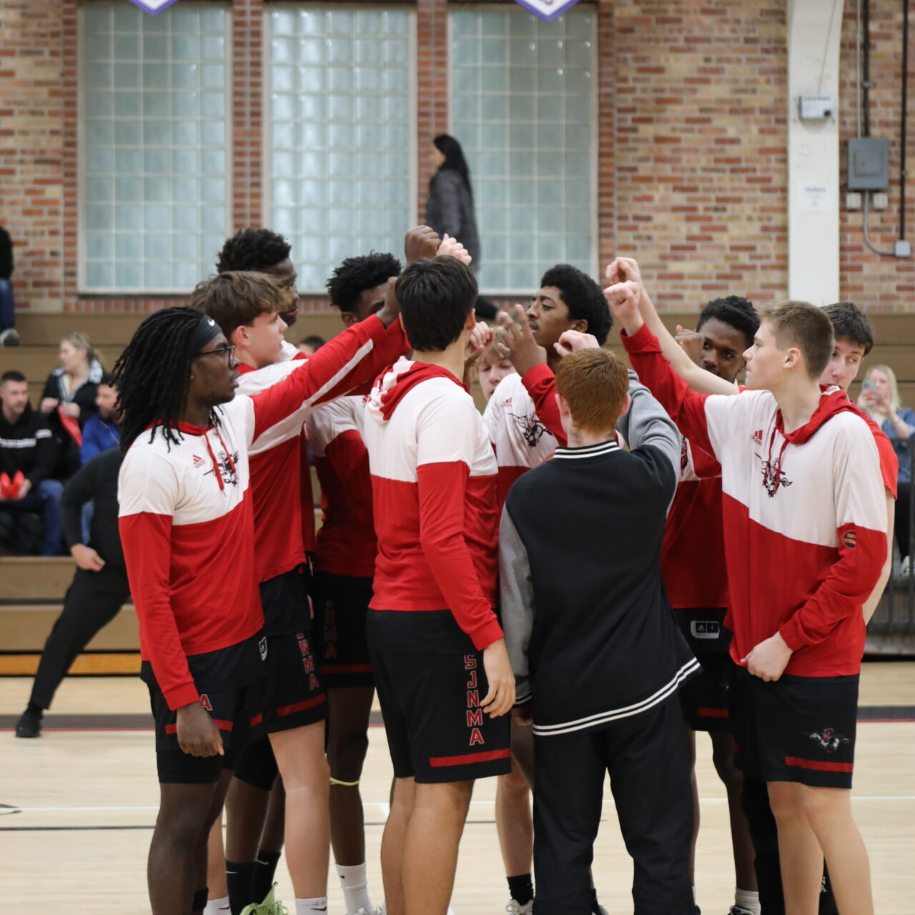 St. John's Northwestern High school Lancers basketball team in red and white uniforms gather in a huddle at center court.