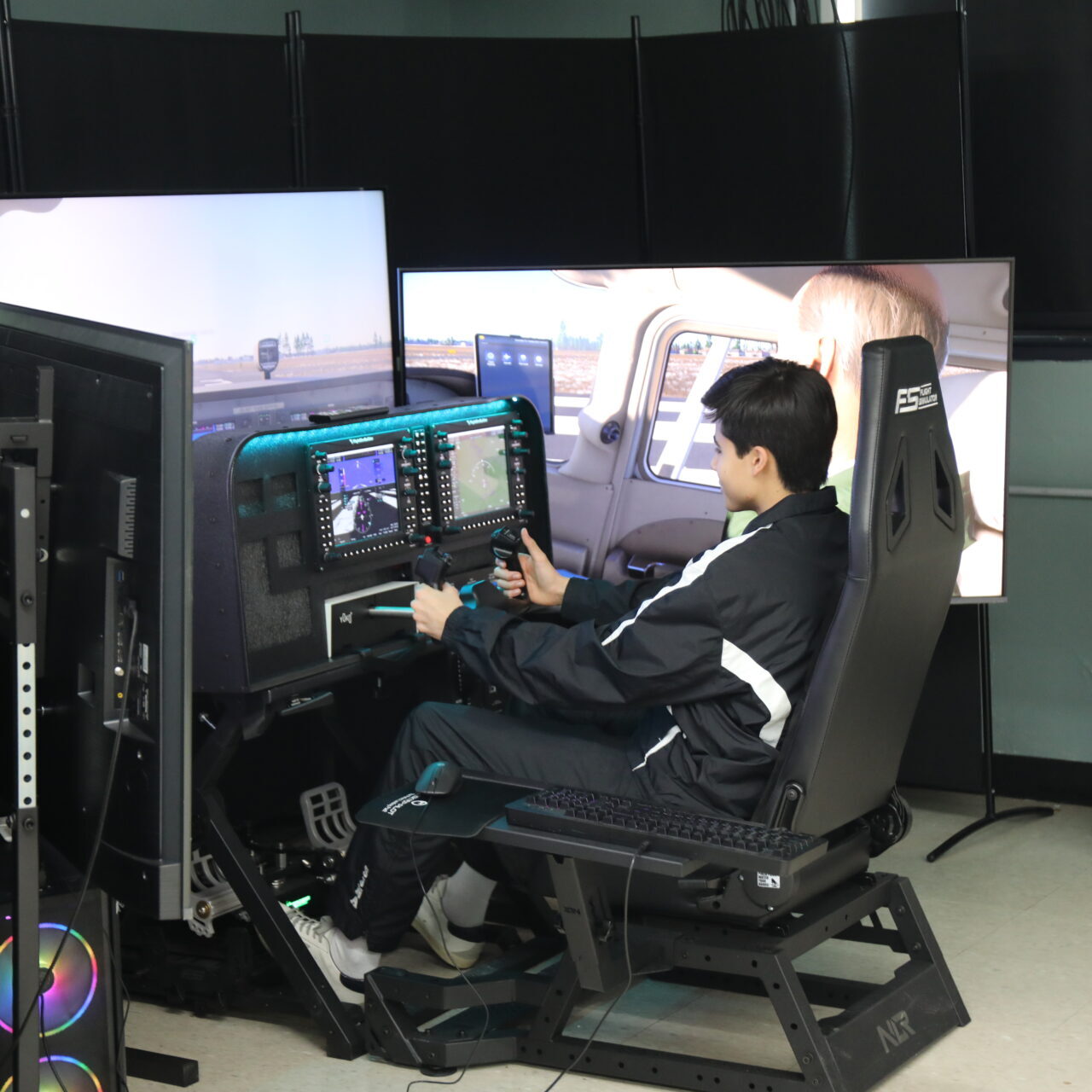 Student sits in a flight simulator cockpit using controls and screens to practice piloting an aircraft in a classroom lab.