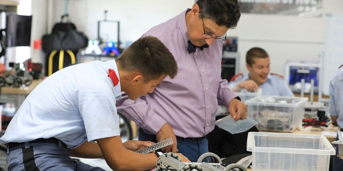 Instructor assists a student in a makerspace classroom as they assemble a robotics project with tools and parts.